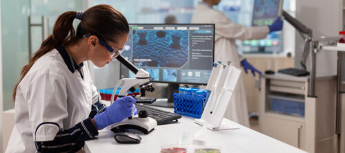 Biotechnology scientist looking through microscope analyzing genetical material. Medicine, biotechnology researcher in advanced pharma lab, examining virus evolution.
