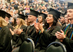 students in cap and gown clap during commencement ceremony